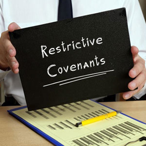 A person holds a “Restrictive Covenants” sign above a clipboard with papers and a yellow pen