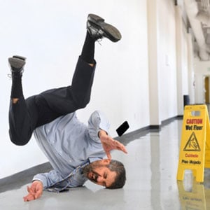  A man falling on his back in an office, slipping on a wet floor.
